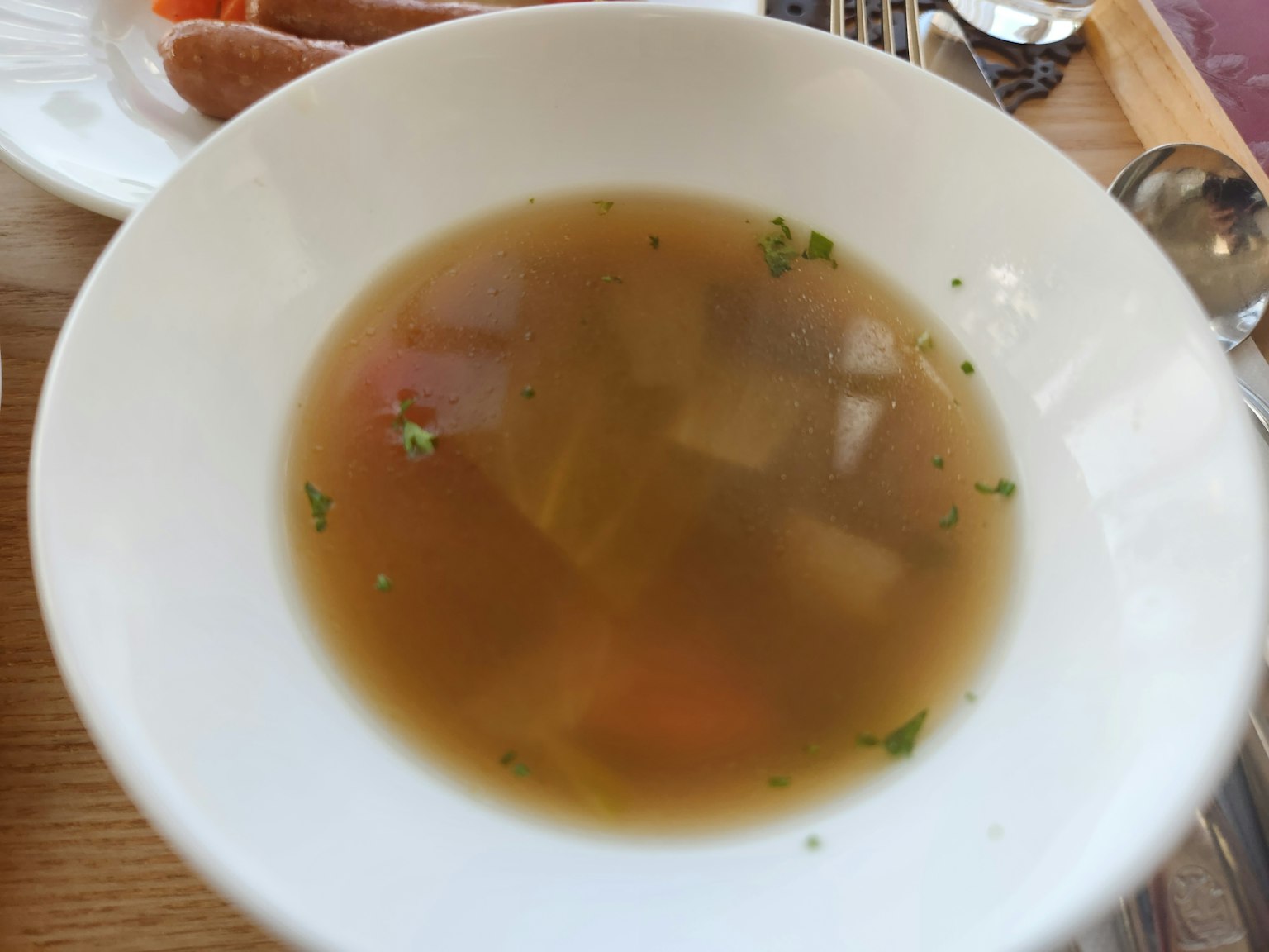 Sopa clara con verduras flotantes en un tazón blanco