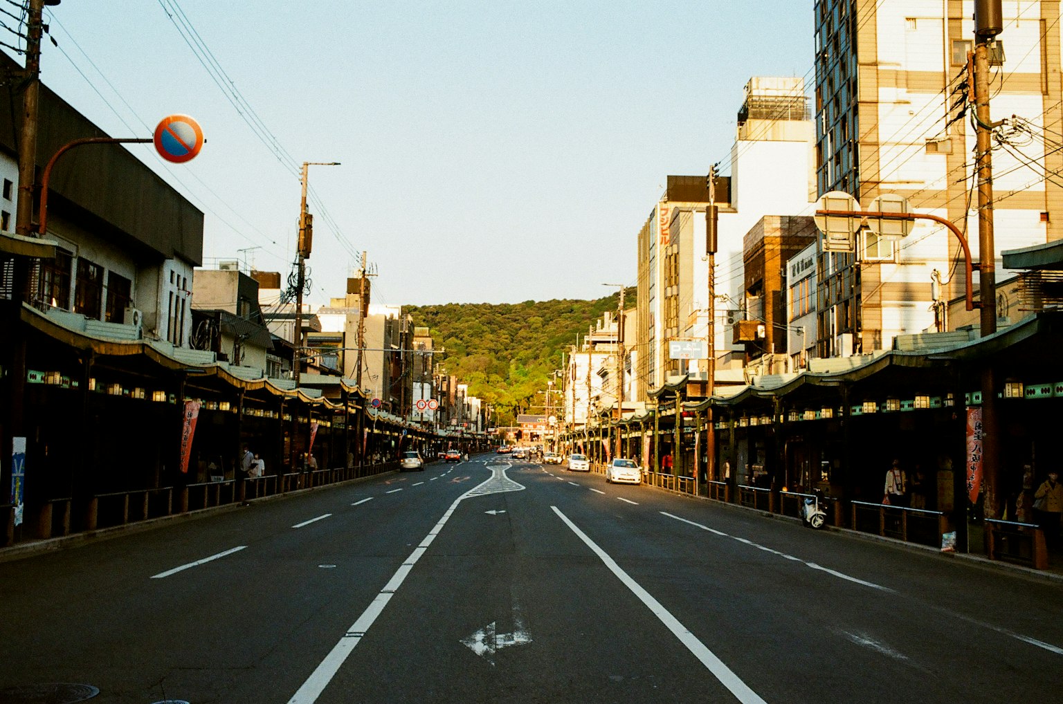 Quiet street scene featuring shops and mountains in the background bathed in soft sunset light