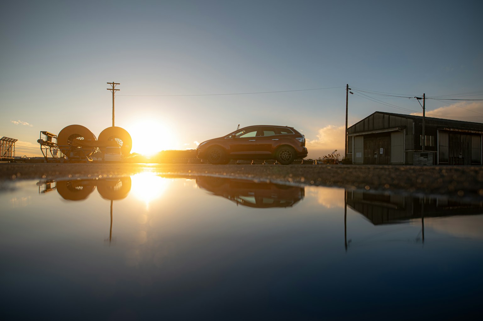 Reflejo del atardecer con un coche y un cobertizo cerca de neumáticos