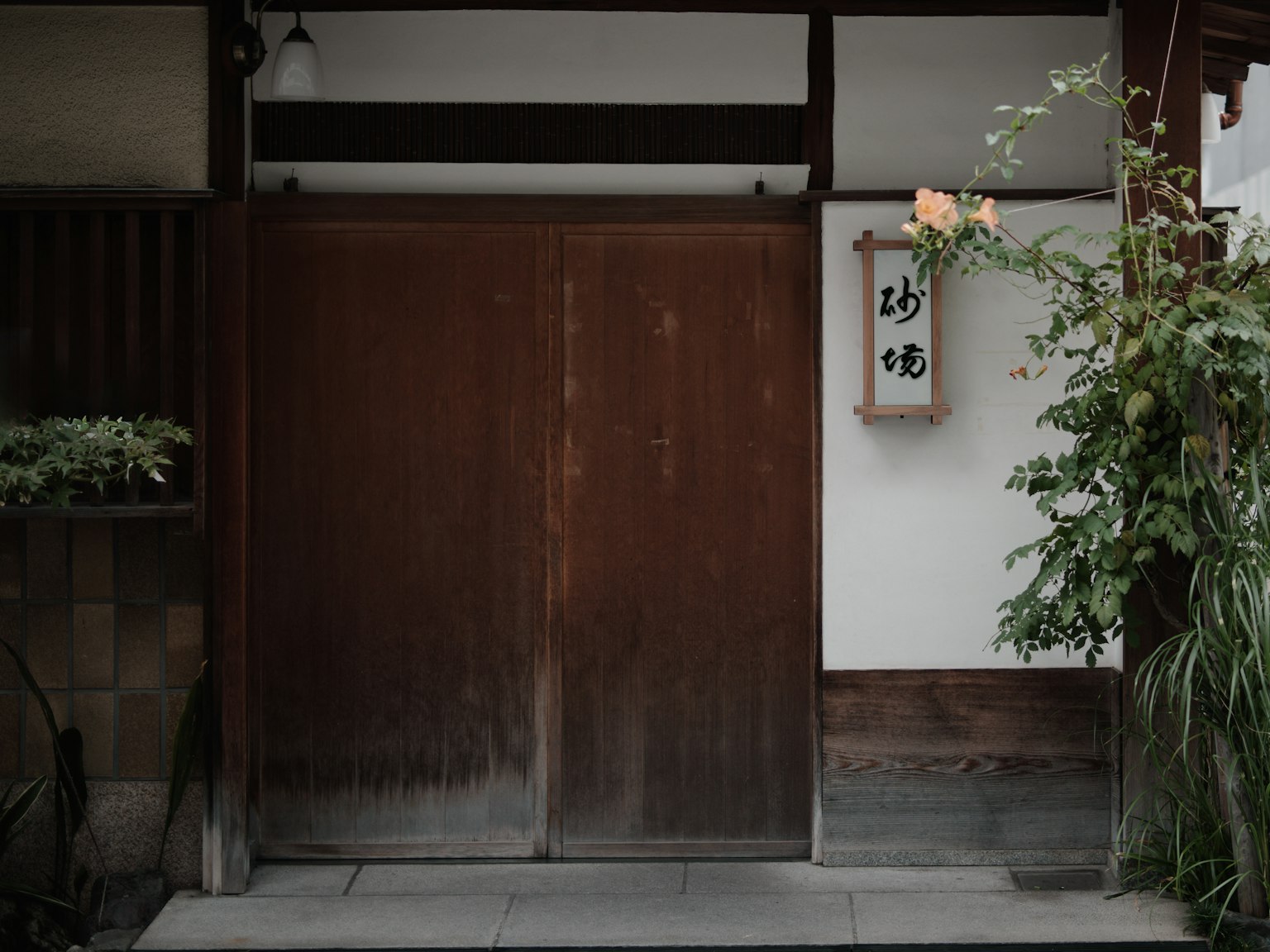 Entrada de una casa japonesa tradicional con puertas de madera y una pared blanca