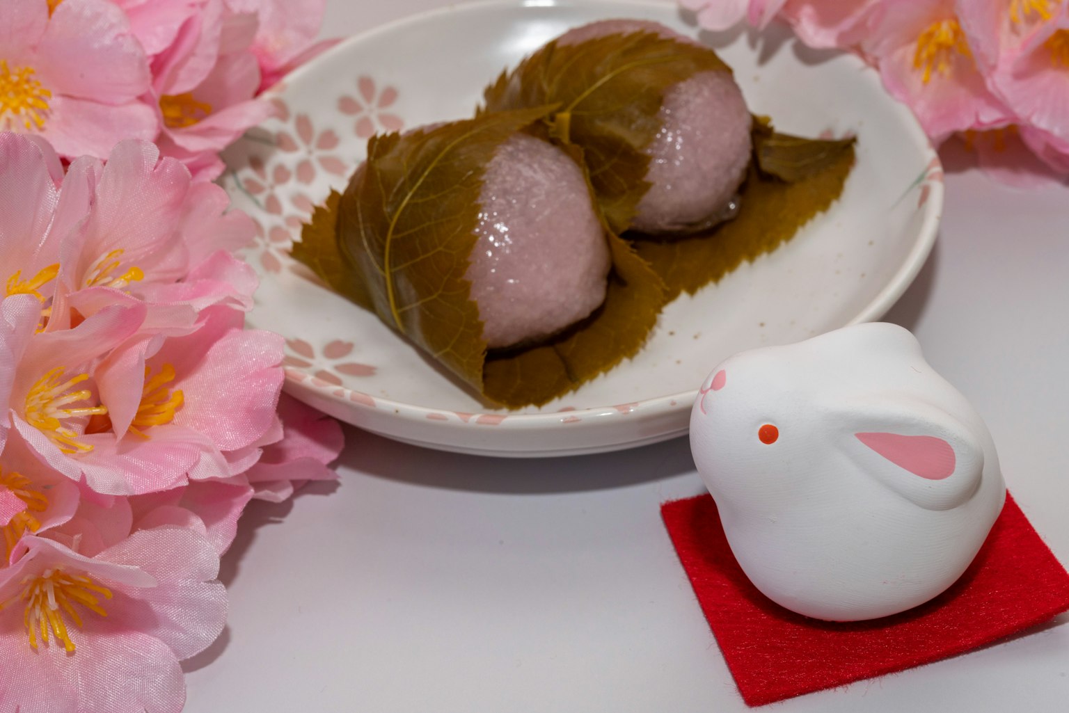 Dos dulces tradicionales japoneses en un plato rodeados de flores de cerezo y un conejito decorativo blanco