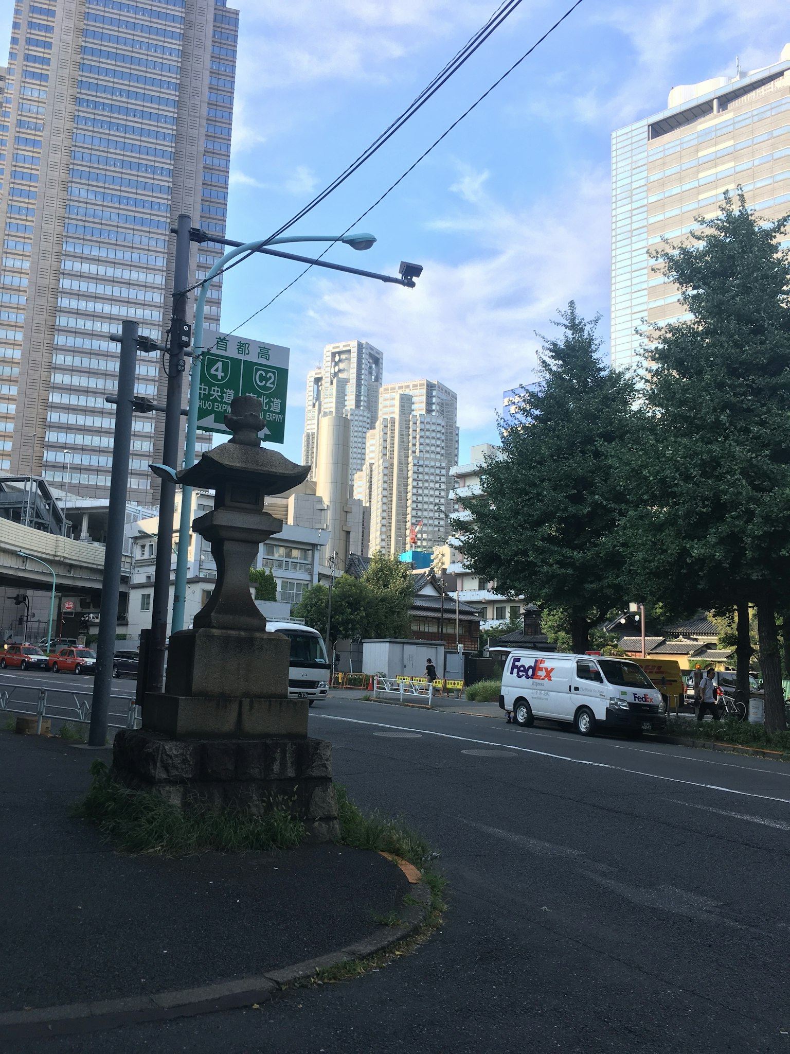 Farol de piedra tradicional en una esquina de la calle rodeado de rascacielos y vegetación