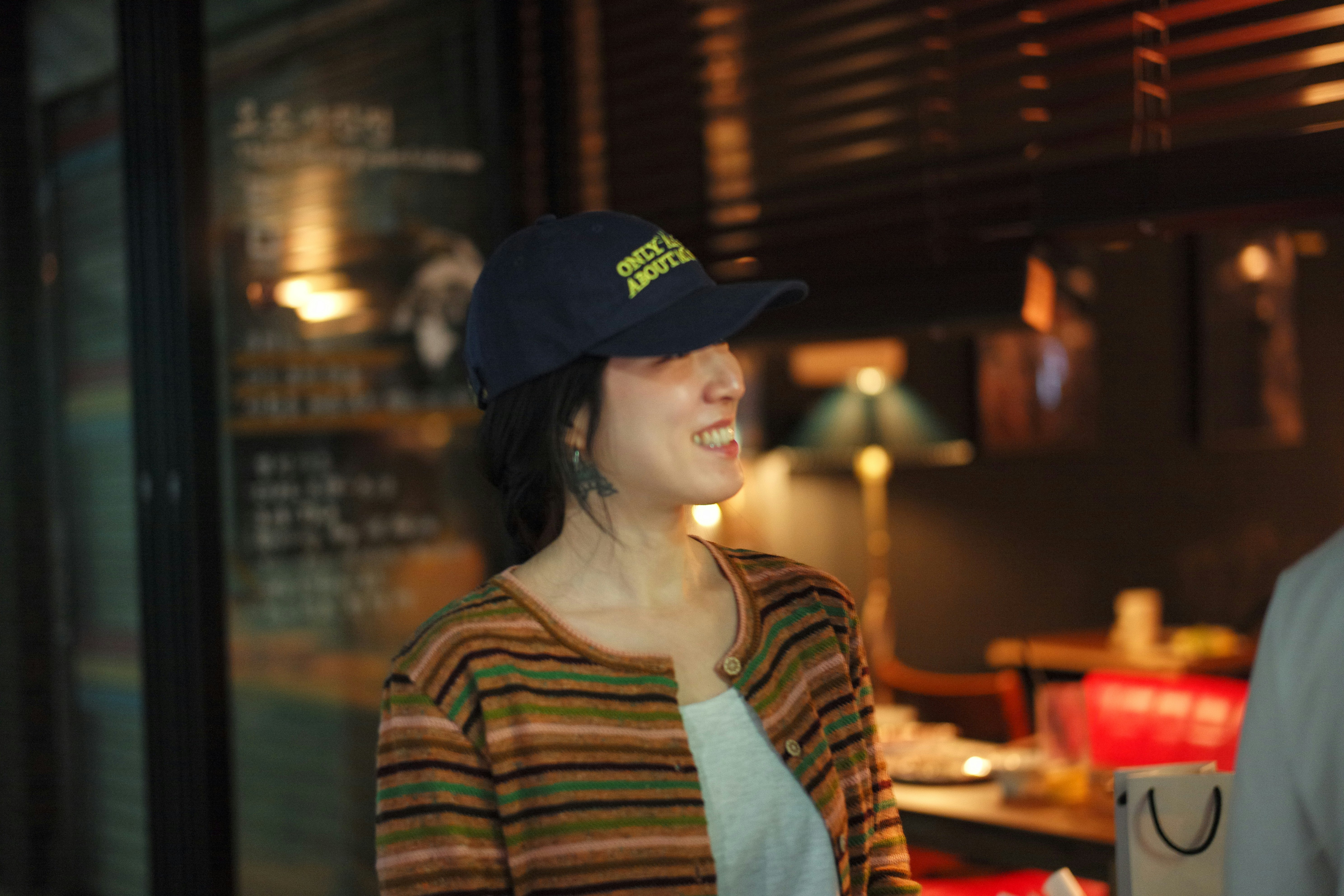 帽子をかぶった女性がカフェの店内で微笑む