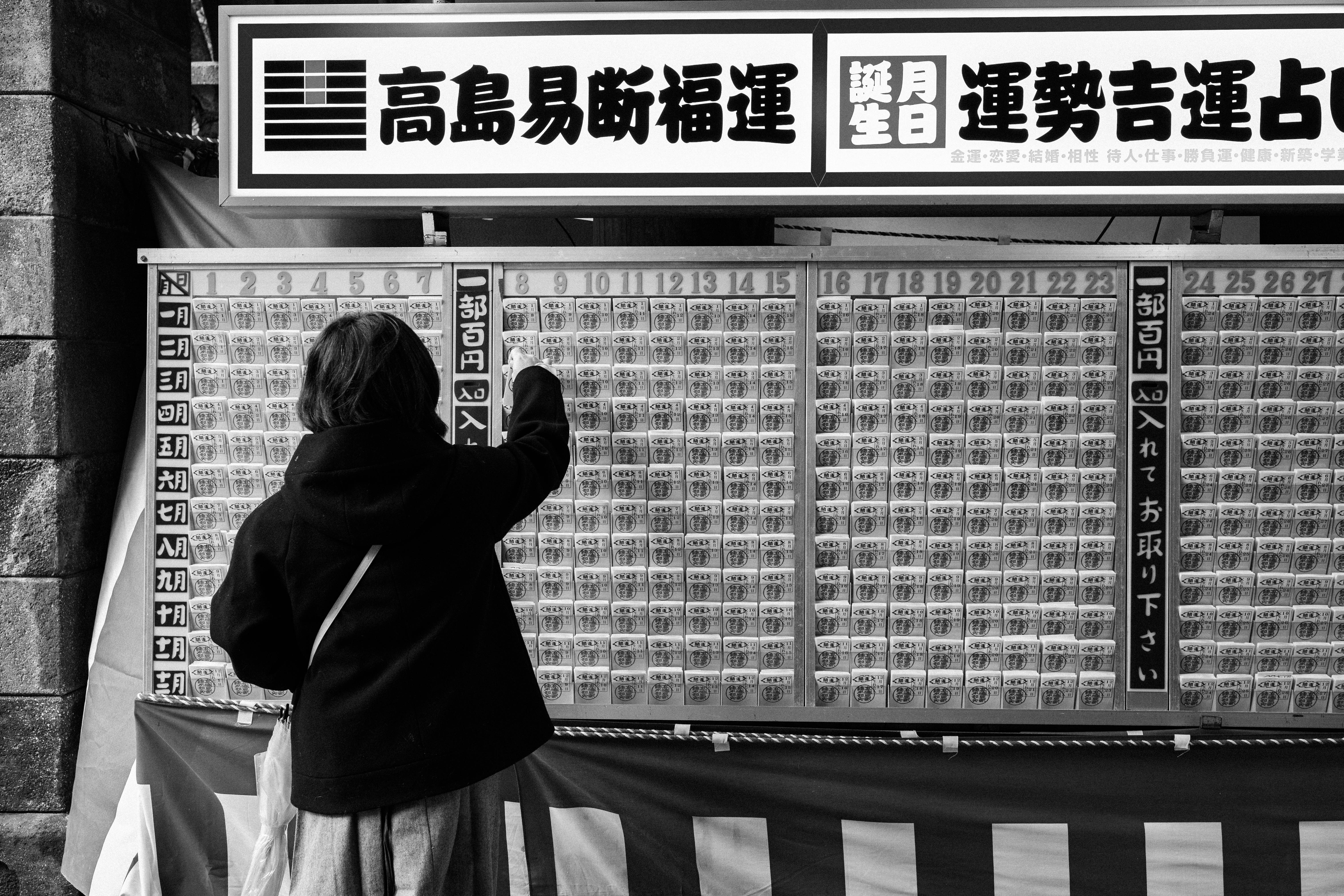 壁に掲示された運勢占いの番号表の前で手を合わせる人物