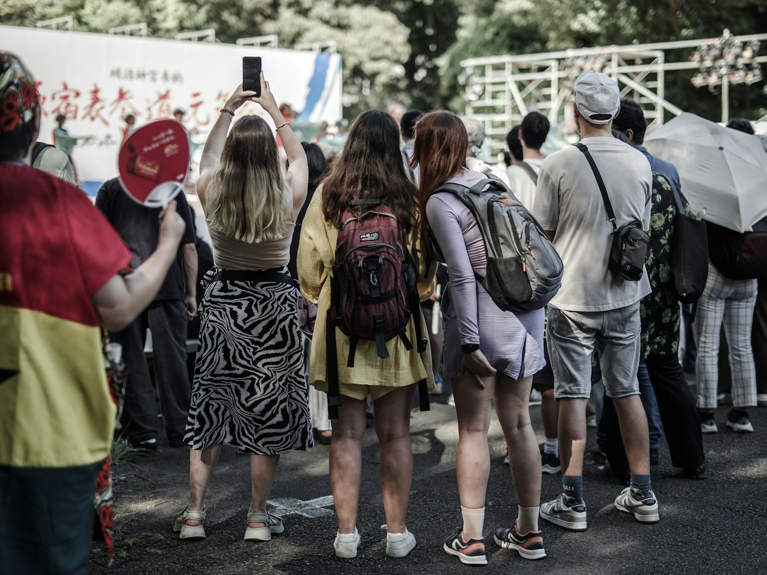 ผู้คนกำลังดูงานอีเวนต์พร้อมผู้เข้าร่วมที่แต่งกายสีสันสดใสอยู่ในพื้นหลัง