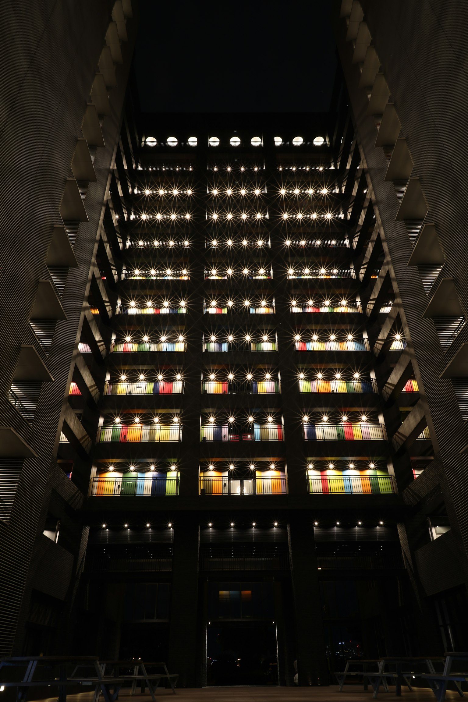Vista nocturna de un edificio con ventanas en niveles iluminadas con vidrios de colores