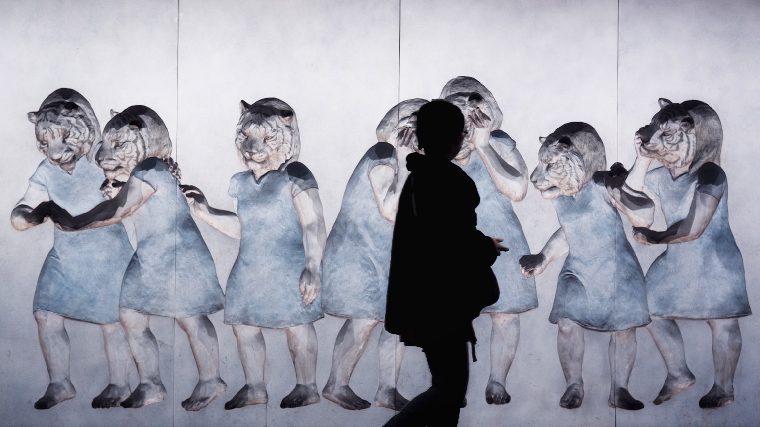 影の人物が青いドレスを着た少女たちの壁画の前に立っている