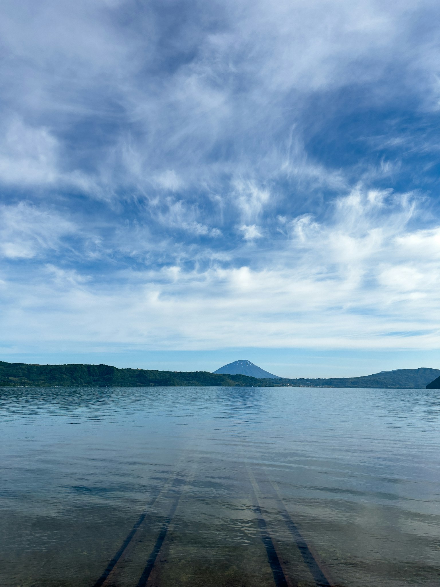 Lac tranquille reflétant des montagnes lointaines sous un ciel bleu
