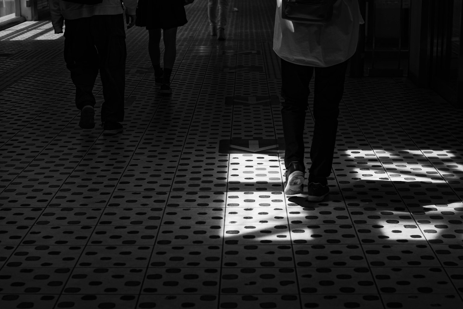 People walking on a tiled floor with contrasting shadows and light