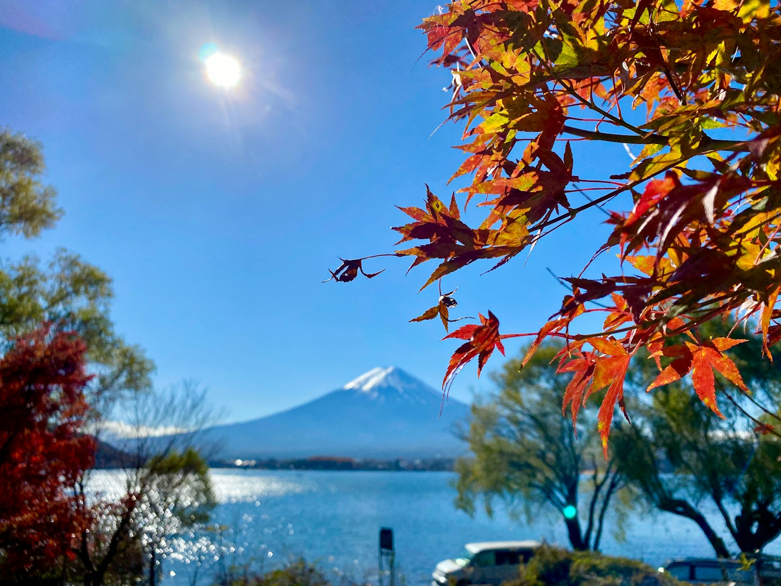 Vista panoramica del monte Fuji e di un lago con foglie autunnali vibranti, cielo blu chiaro e sole splendente