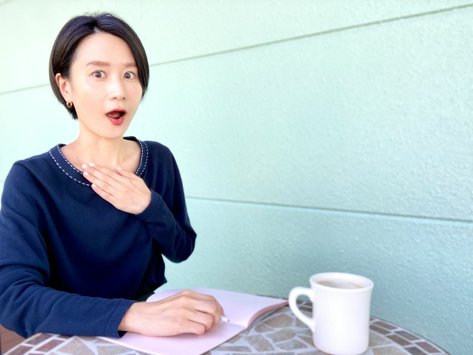 一位惊讶的女性坐在桌子旁，手里拿着咖啡杯，正在笔记本上写字