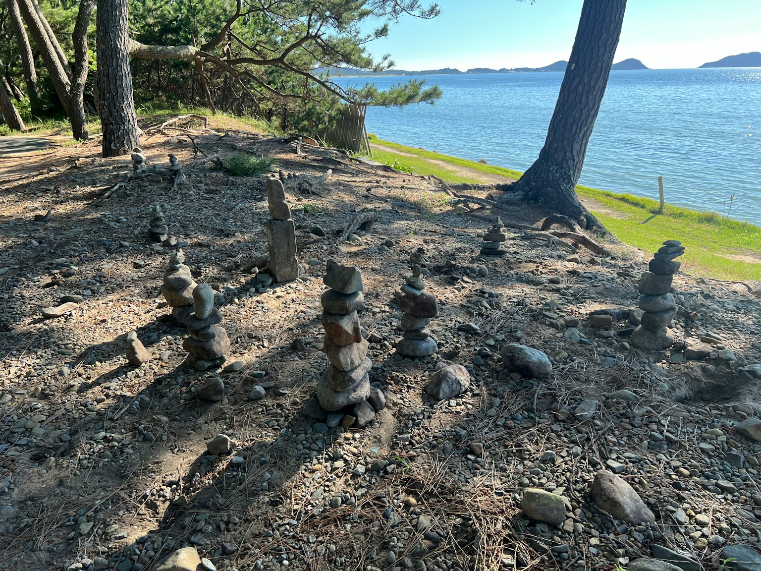 海岸沿いの木々の間に積まれた石のアート作品が並ぶ風景