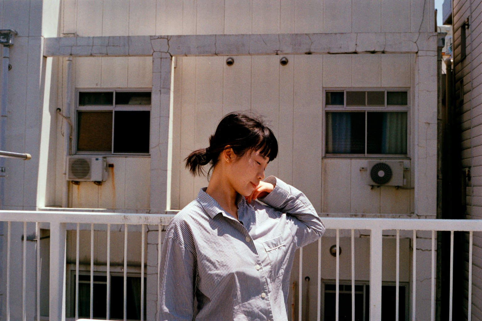 A woman wearing a gray shirt outdoors with a white building and windows in the background