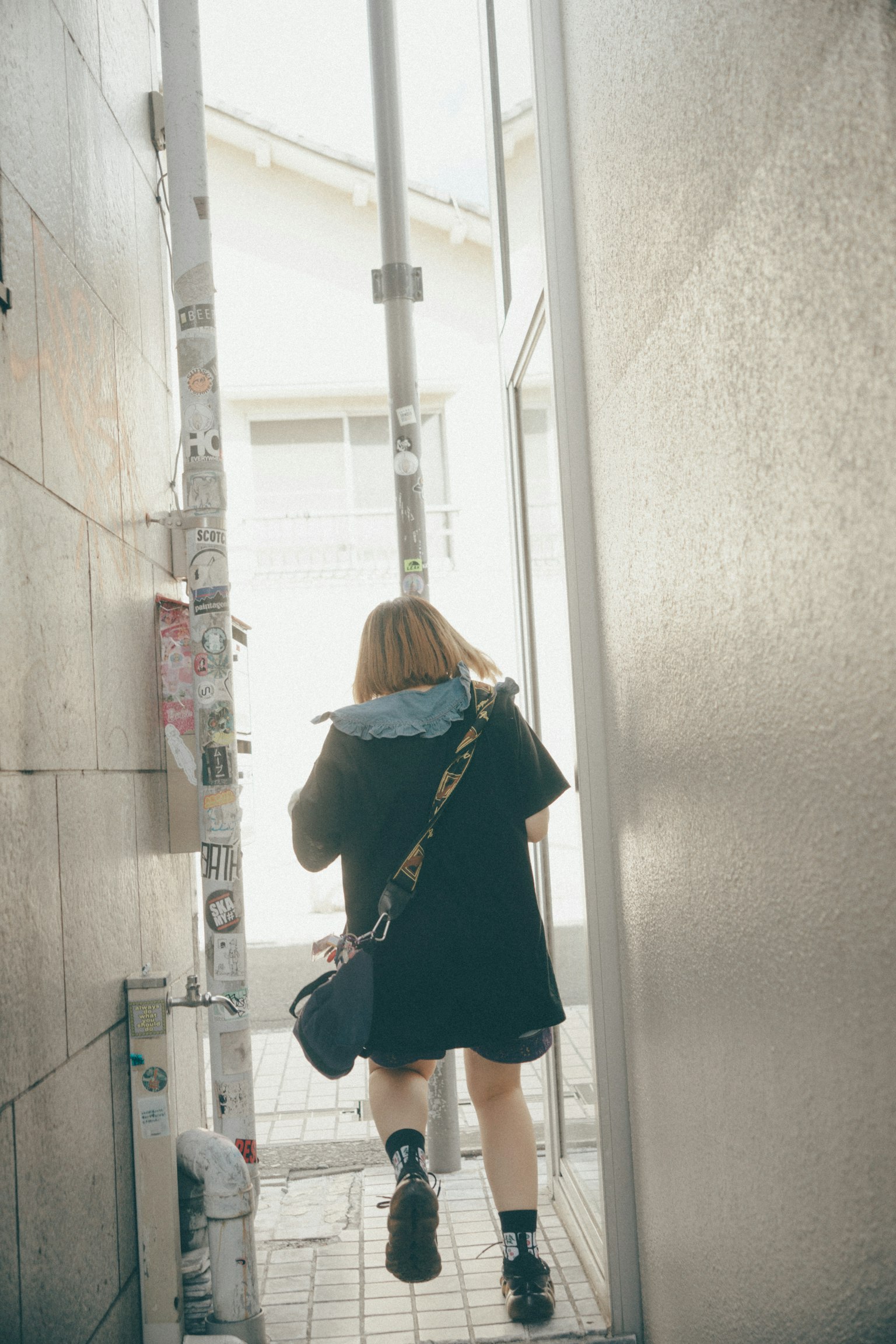 좁은 통로를 걷고 있는 여성 그녀는 검은 코트를 입고 있으며 등 뒤에 가방을 메고 있다
