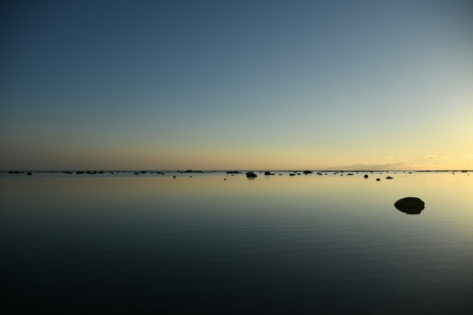 Calm water surface with small rocks at dusk over the sea