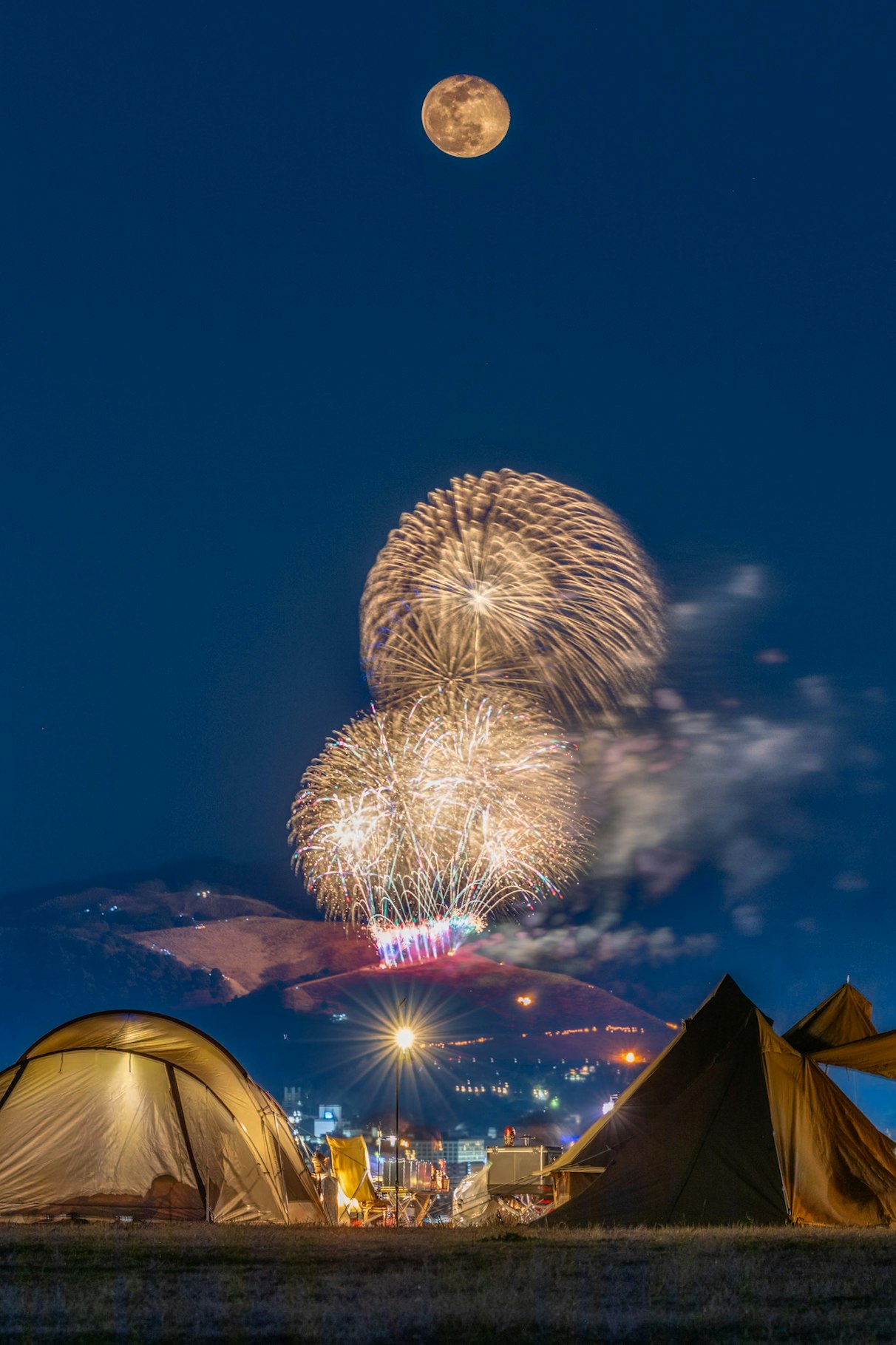 満月の夜に花火が上がるキャンプ場のテント群