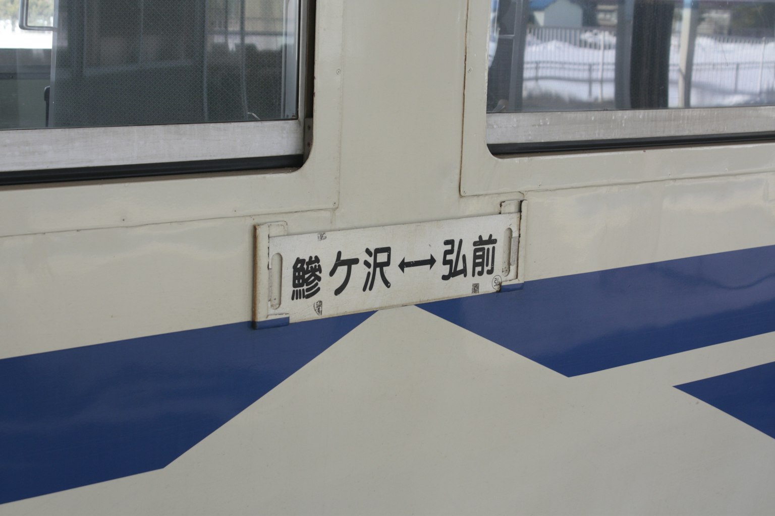 Jendela kereta dengan papan nama stasiun dan garis biru