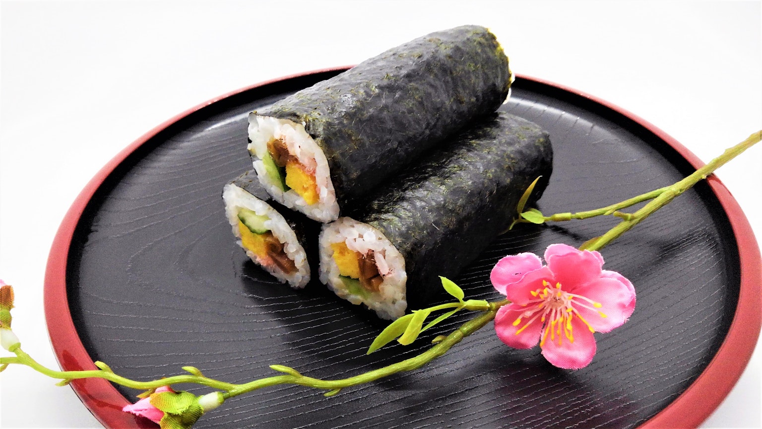 Ba cuộn sushi được bọc trong rong biển đen trên đĩa có trang trí hoa