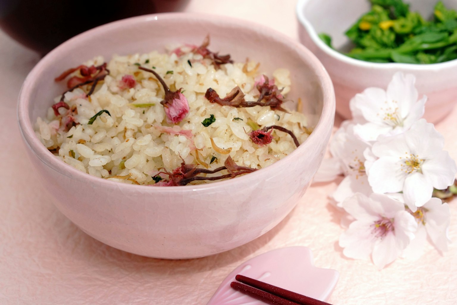 Bol de riz avec des fleurs de cerisier et un petit plat d'herbes vertes