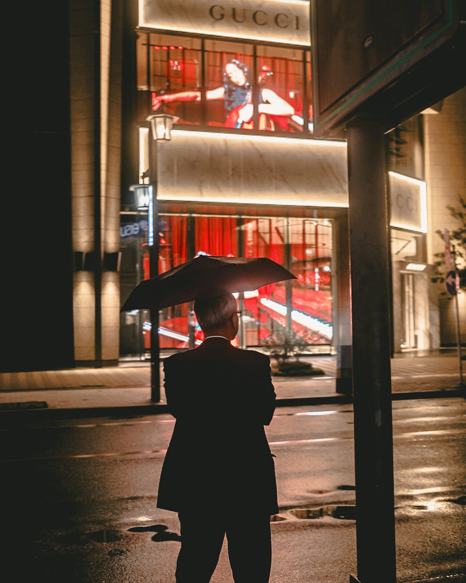 Ein Mann mit einem Regenschirm steht nachts vor einem Gucci-Geschäft