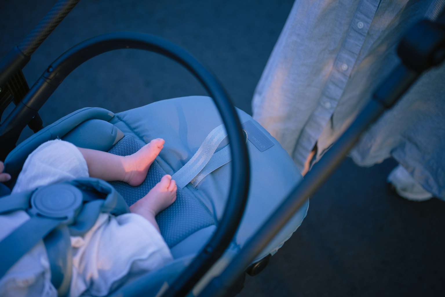 Füße eines Babys in einem blauen Kinderwagen mit Füßen eines Erwachsenen in der Nähe