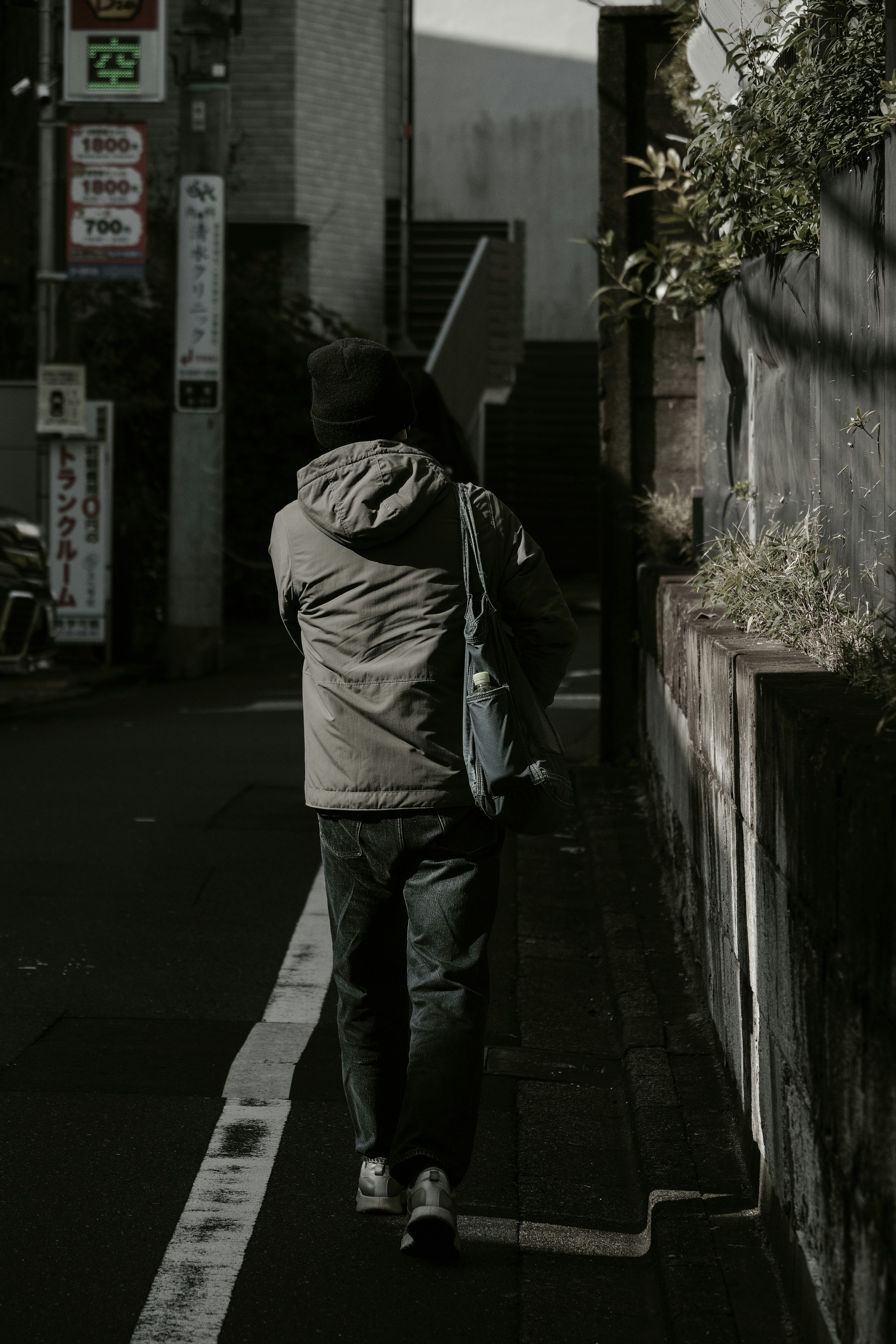 路地の壁際を歩く人物とトートバッグのある街並み