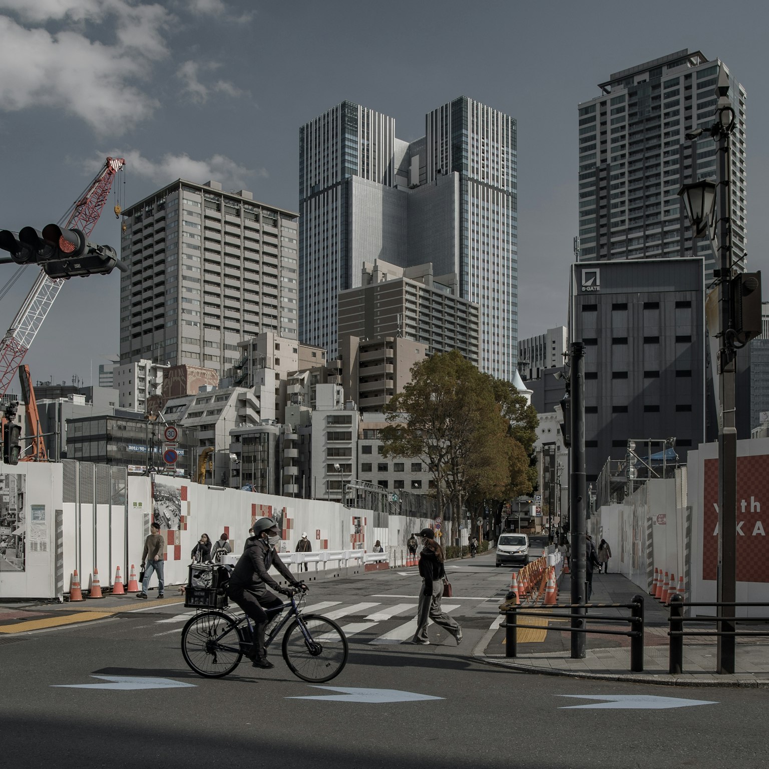 Intersección urbana con un ciclista y peatones Edificios altos y un sitio de construcción al fondo