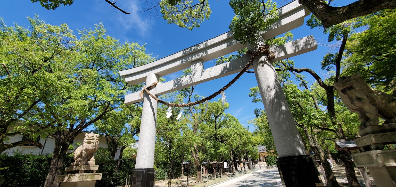 Cổng torii lớn dưới bầu trời xanh được bao quanh bởi cây cối xanh tươi