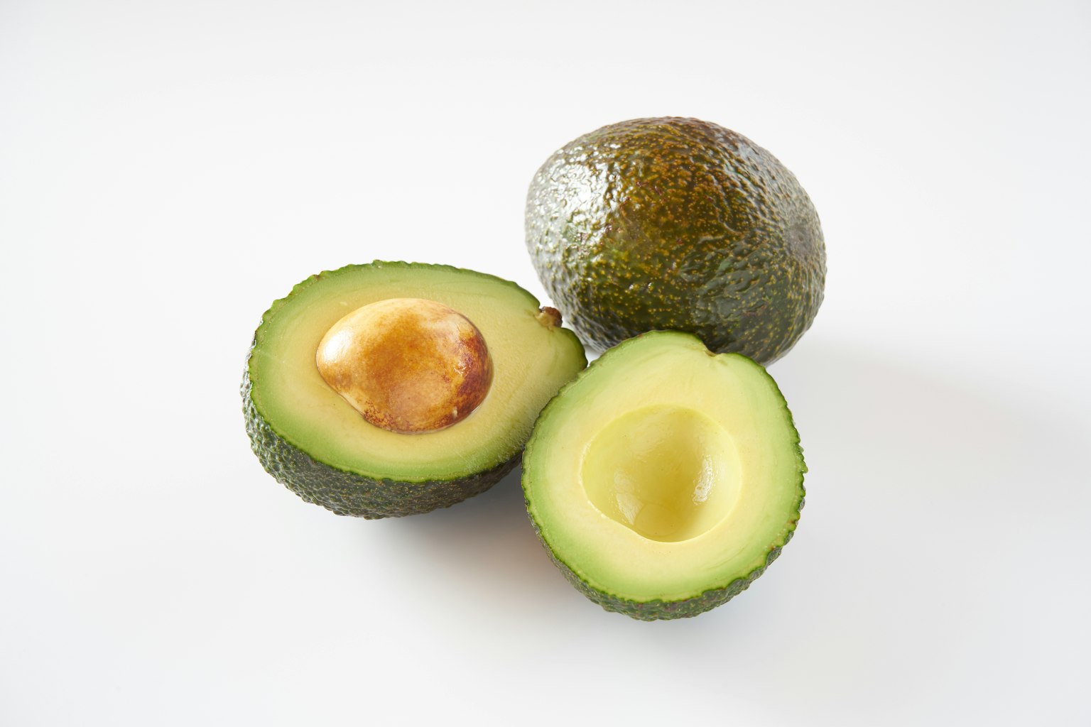Ganzes und halbiertes Avocado mit sichtlichem Kern auf weißem Hintergrund