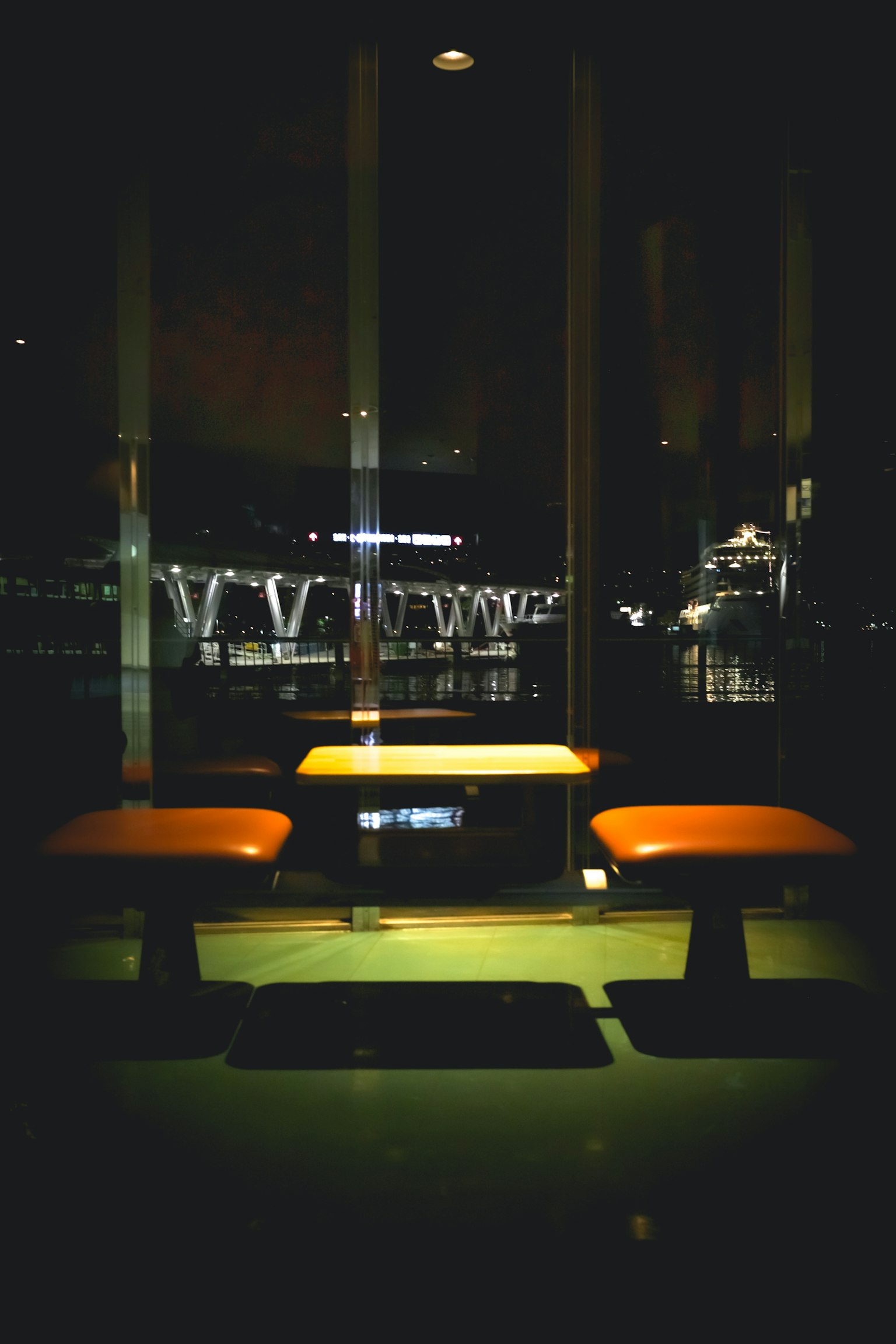 暗い背景に明るいオレンジ色の椅子があるテーブルの画像 窓の外には夜景が広がる