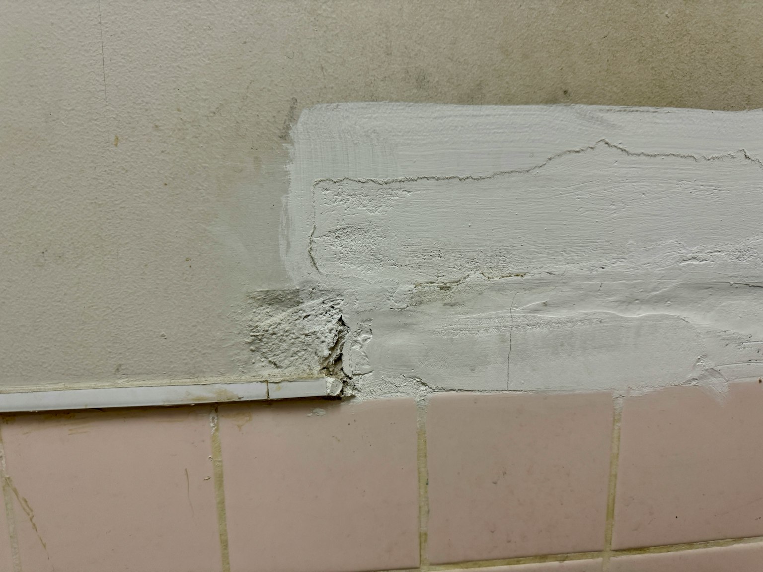 Ein Abschnitt einer Wand mit einem gestrichenen weißen Bereich, der eine rissige Textur zeigt