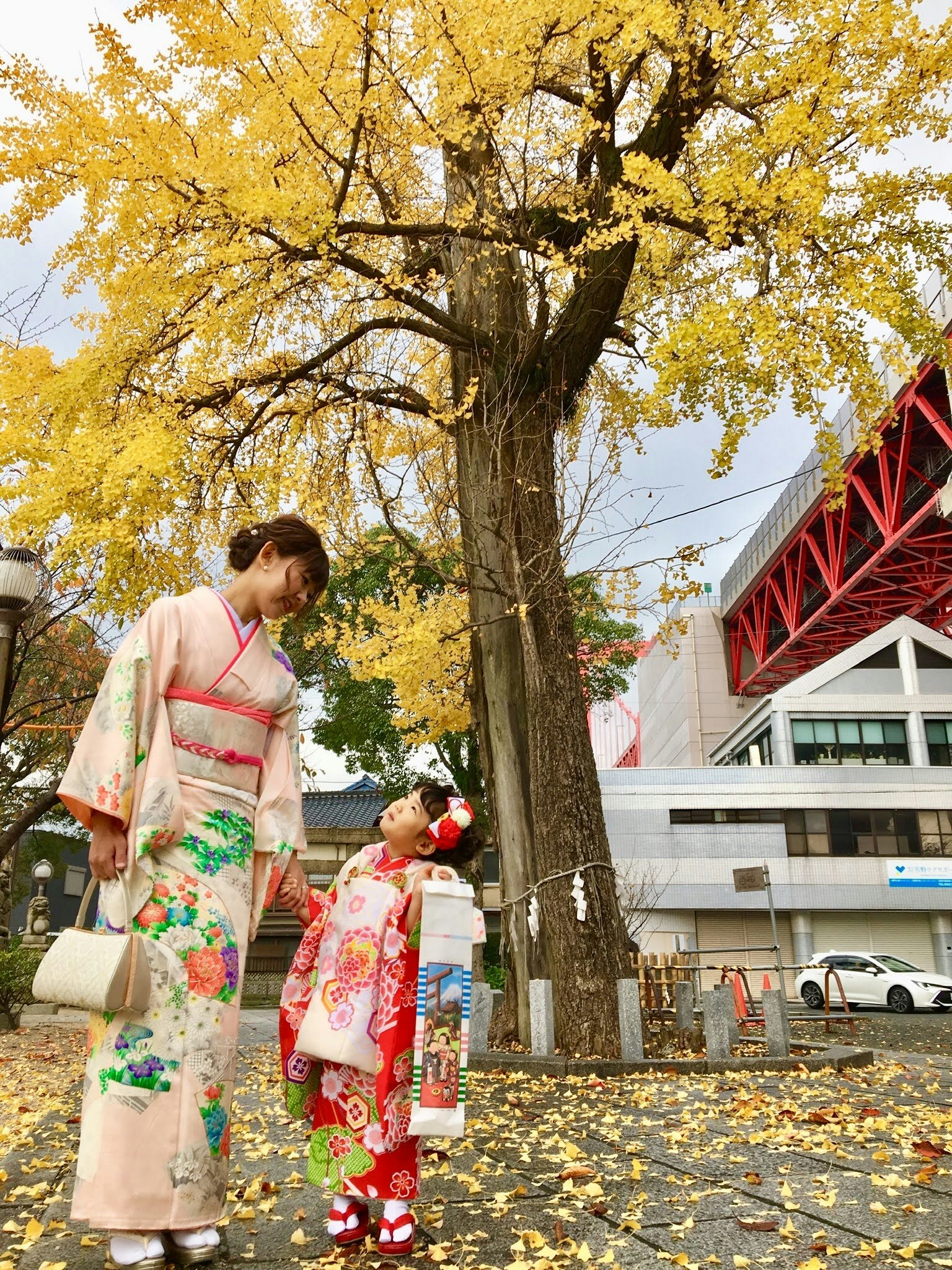 Una madre y su hija en kimonos tradicionales mirándose bajo hojas amarillas de otoño