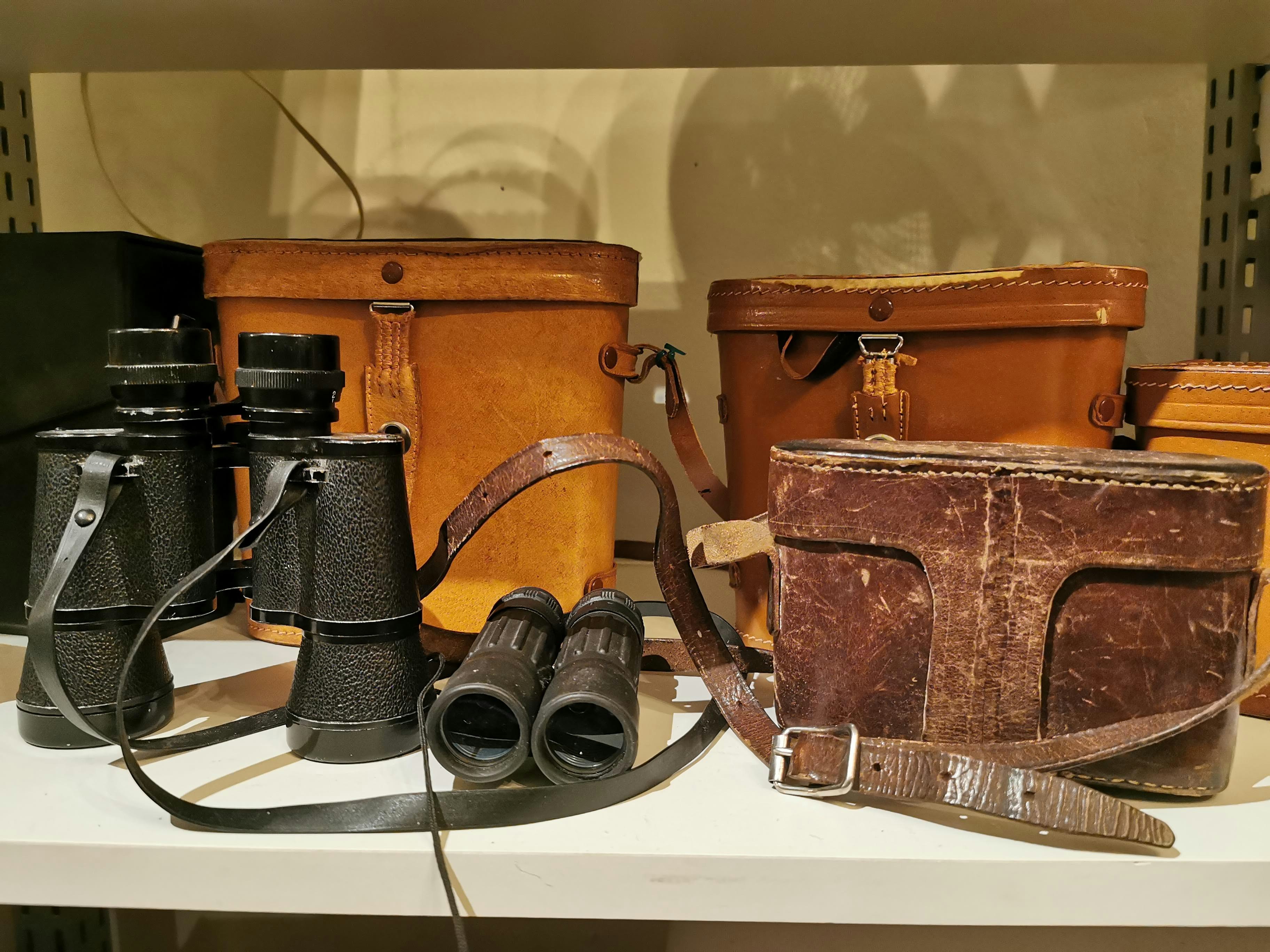 革のカメラバッグとレトロな双眼鏡、フィルムカメラ周辺小物のある机上