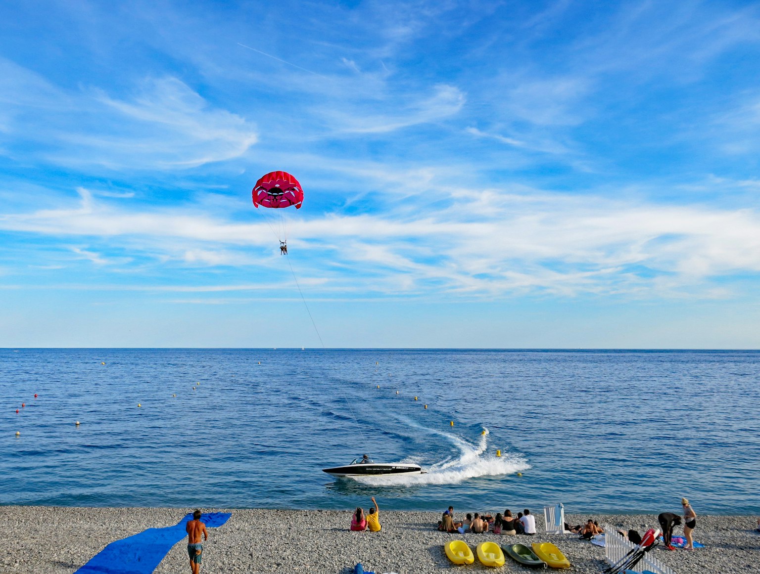 Pemandangan pantai dengan parasailing dan perahu di bawah langit biru