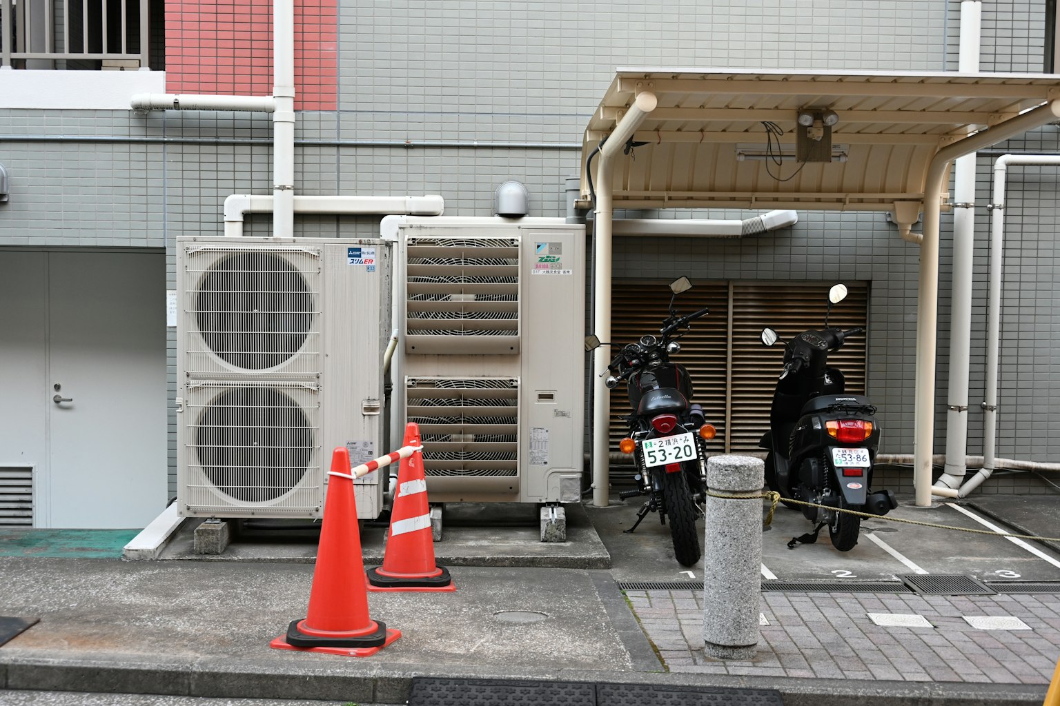 Scène avec une unité de climatisation et deux motos garées des cônes orange sont alignés dans la zone de stationnement