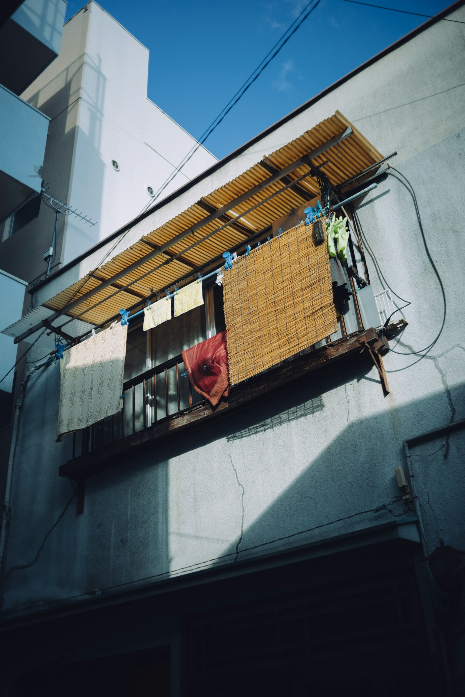 Balkon apartemen di bawah langit biru dengan pakaian yang digantung dan tikar bambu