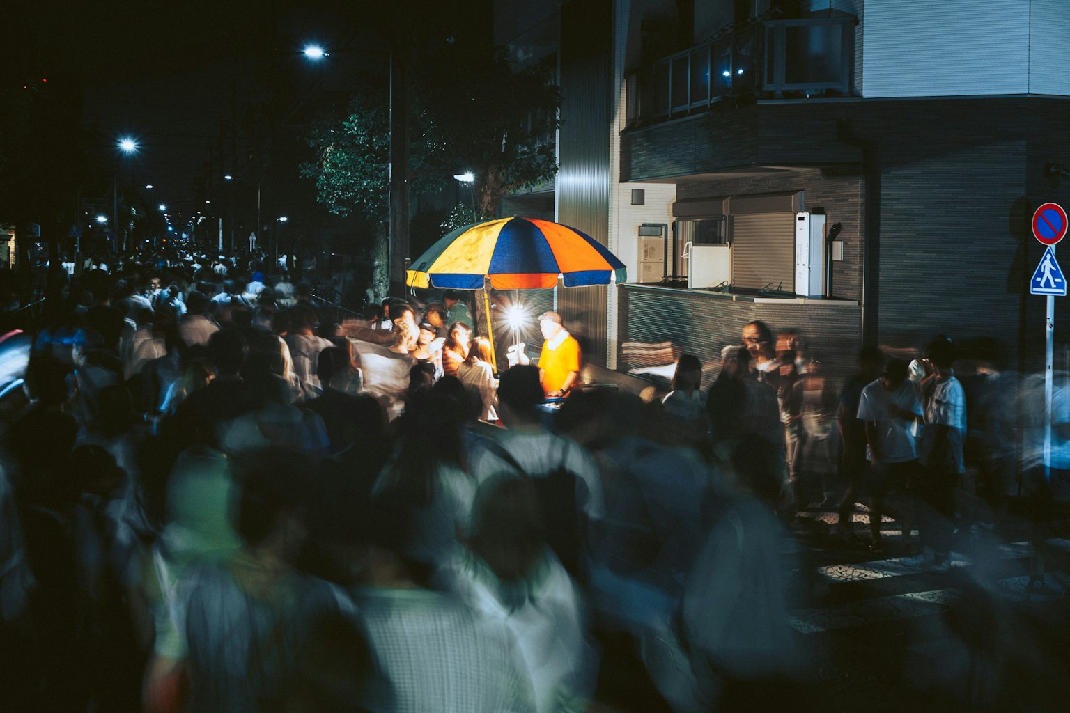 Folla di persone in una strada affollata di notte con un chiosco di cibo colorato