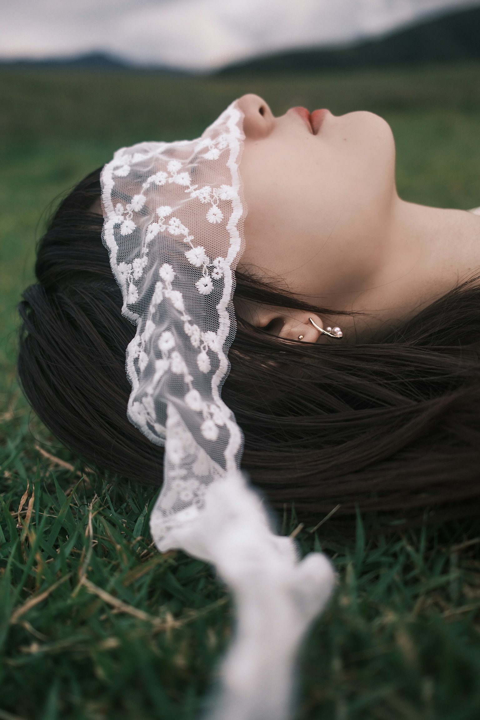 草の上に横たわる女性の顔にレースの布がかかっている