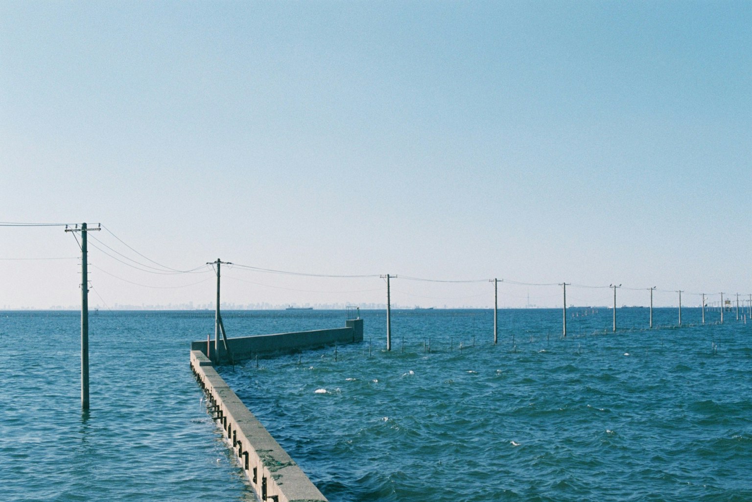 Muelle con postes eléctricos sobre el océano azul bajo un cielo claro