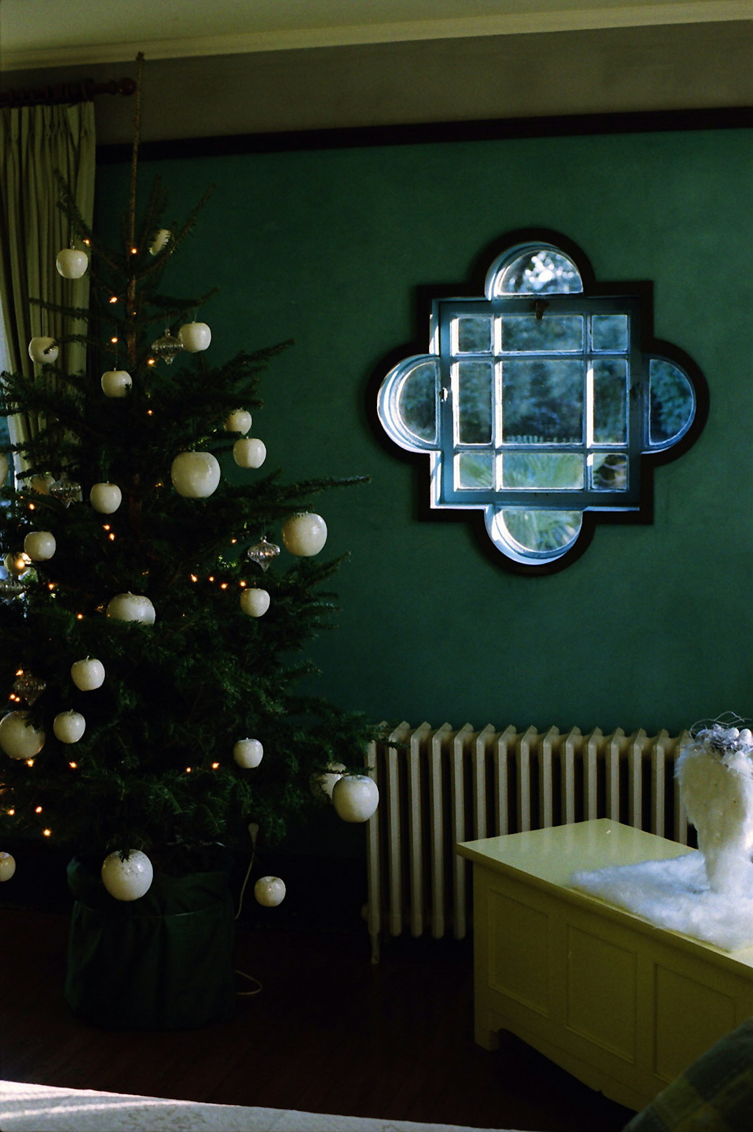 Zimmer mit einem Weihnachtsbaum, der mit weißen Ornamenten dekoriert ist, und einem dekorativen Spiegel an einer grünen Wand