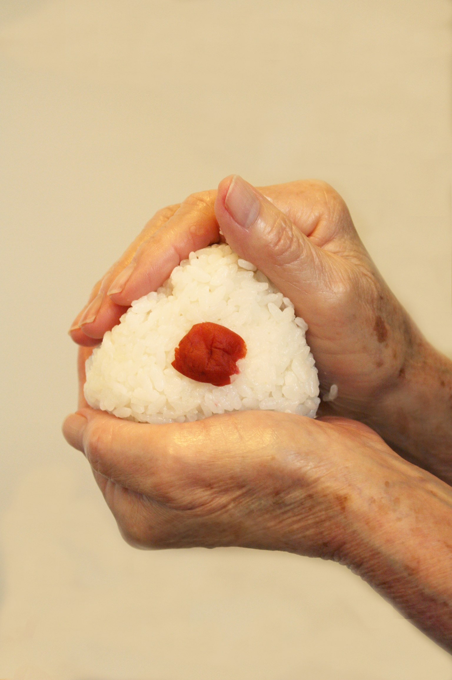 Mains formant un onigiri avec un umeboshi rouge au centre