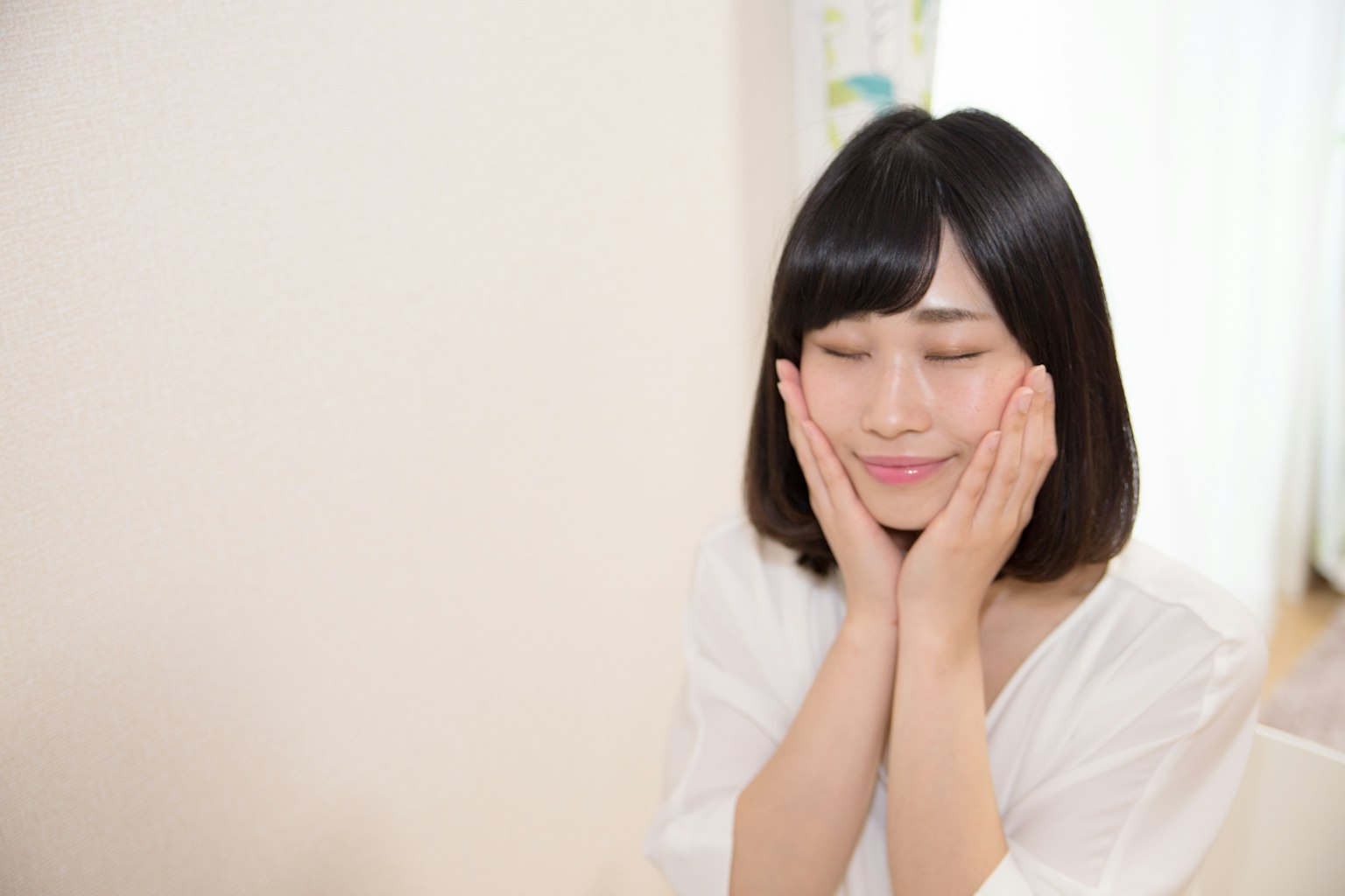 A woman smiling with her hands on her face in a bright indoor setting