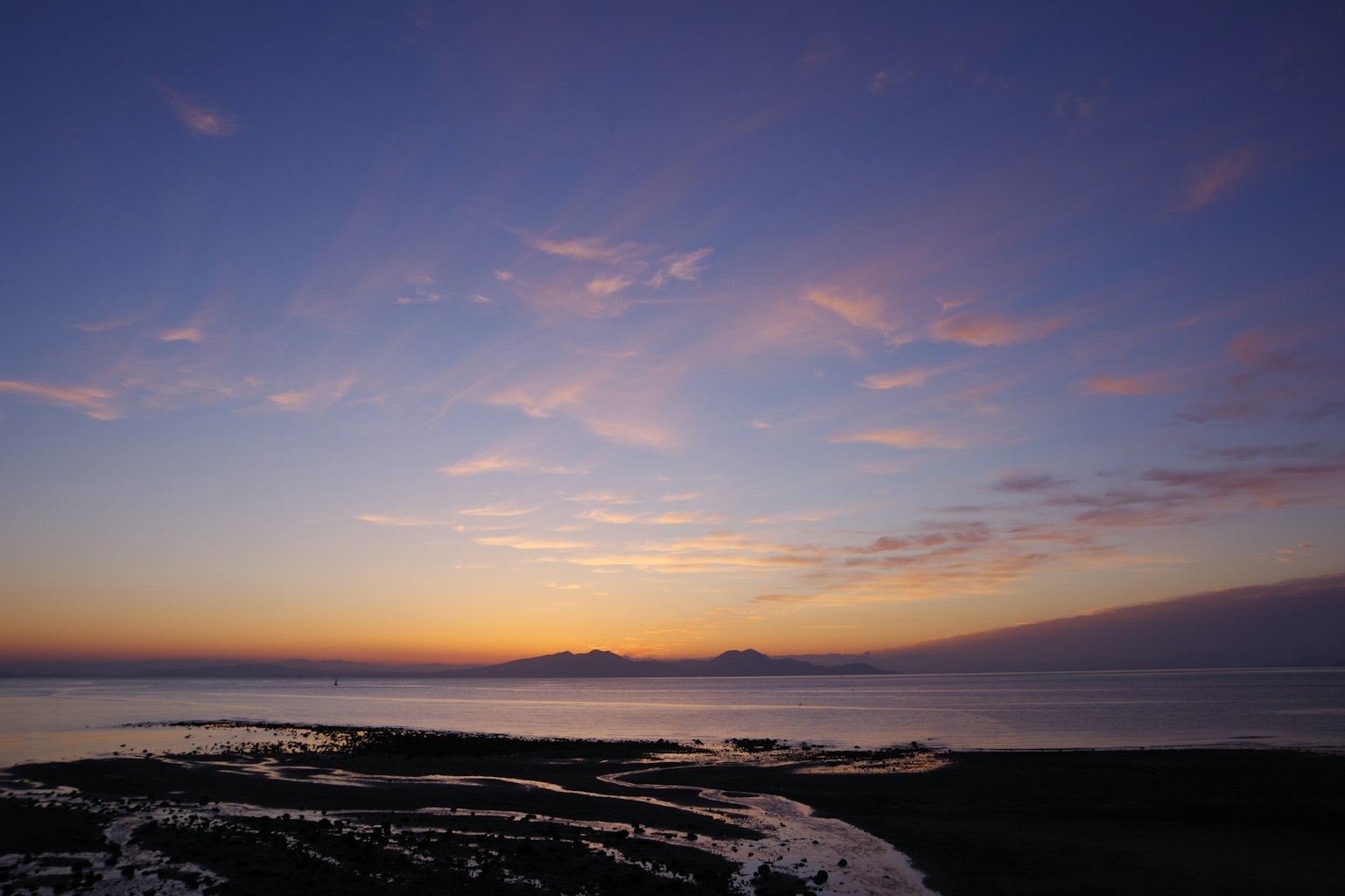 Schöner Sonnenuntergang über dem Meer mit lila und orangefarbenen Abstufungen und fernen Bergen