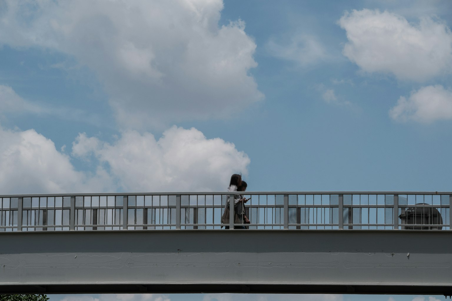 Silhouette of a person walking on a bridge under a blue sky