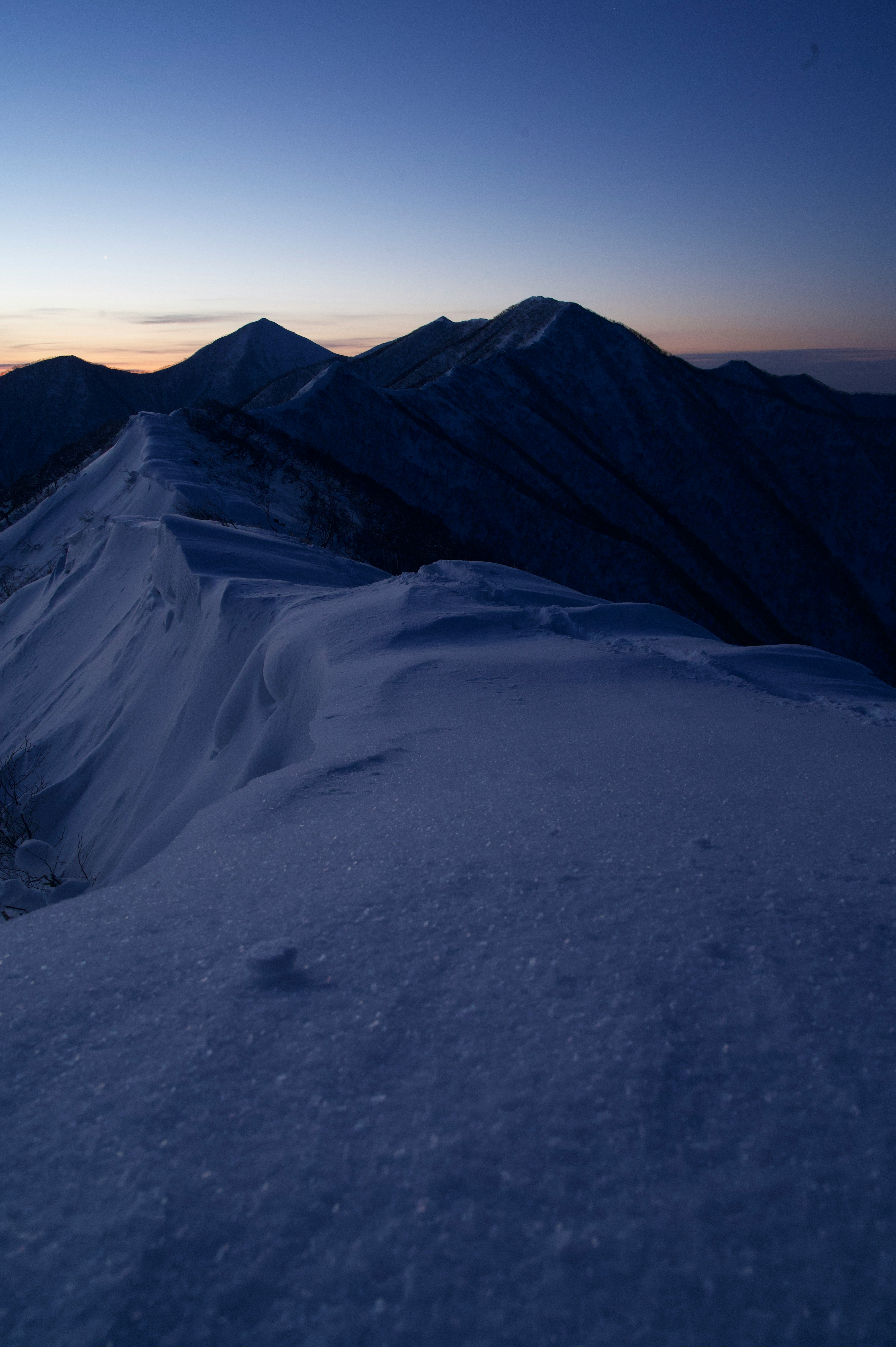 夜明け前の雪山の稜線と広がる斜面