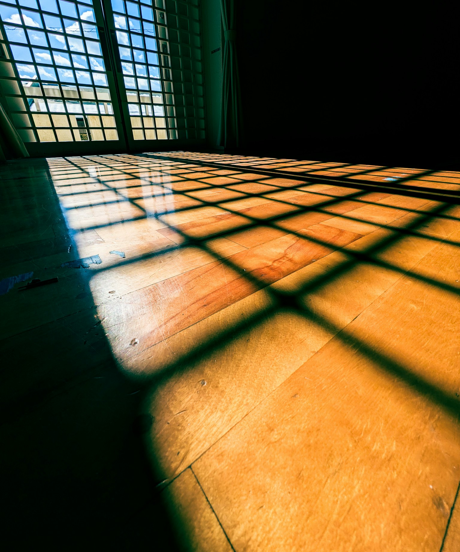 Interior scene with sunlight casting grid-like shadows on the wooden floor