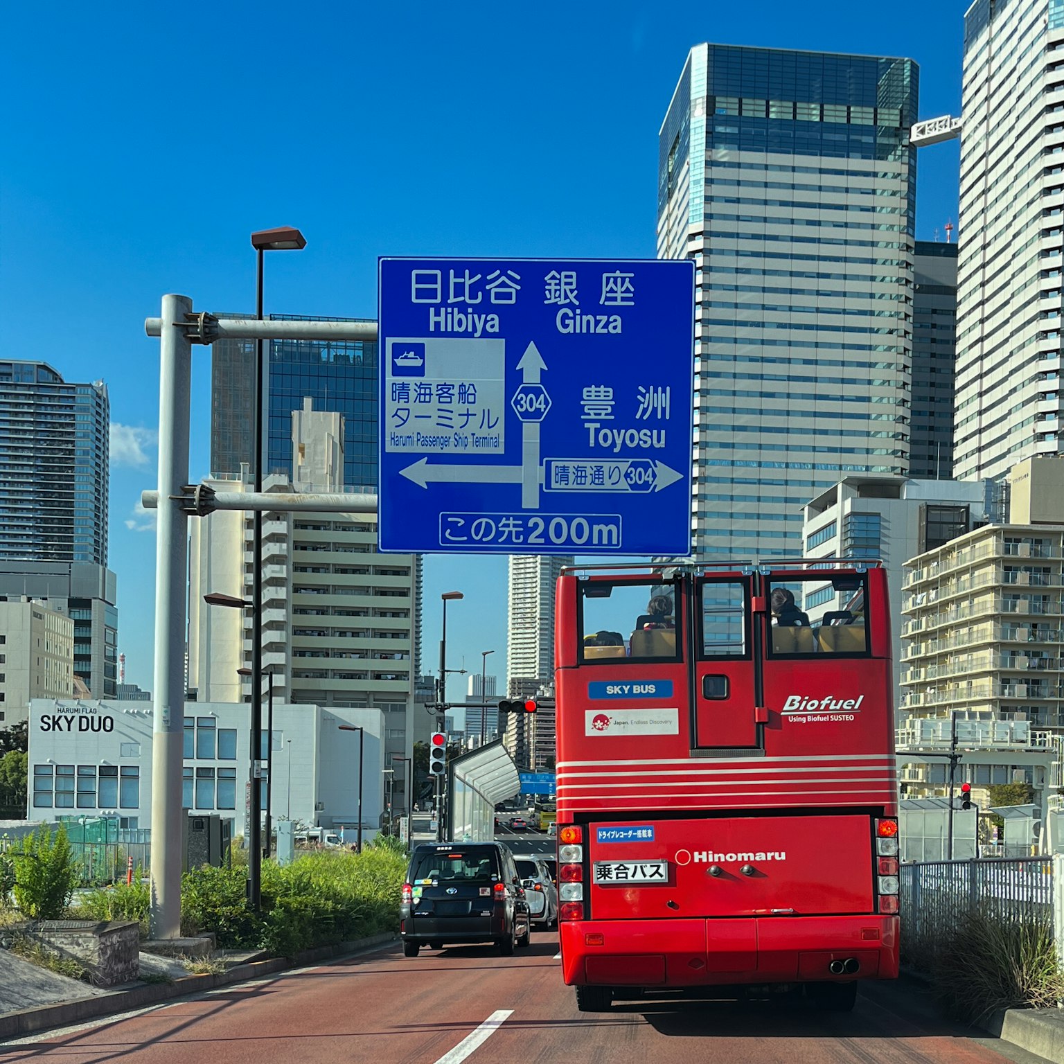 Autobús turístico rojo circulando por una carretera de la ciudad con rascacielos de fondo
