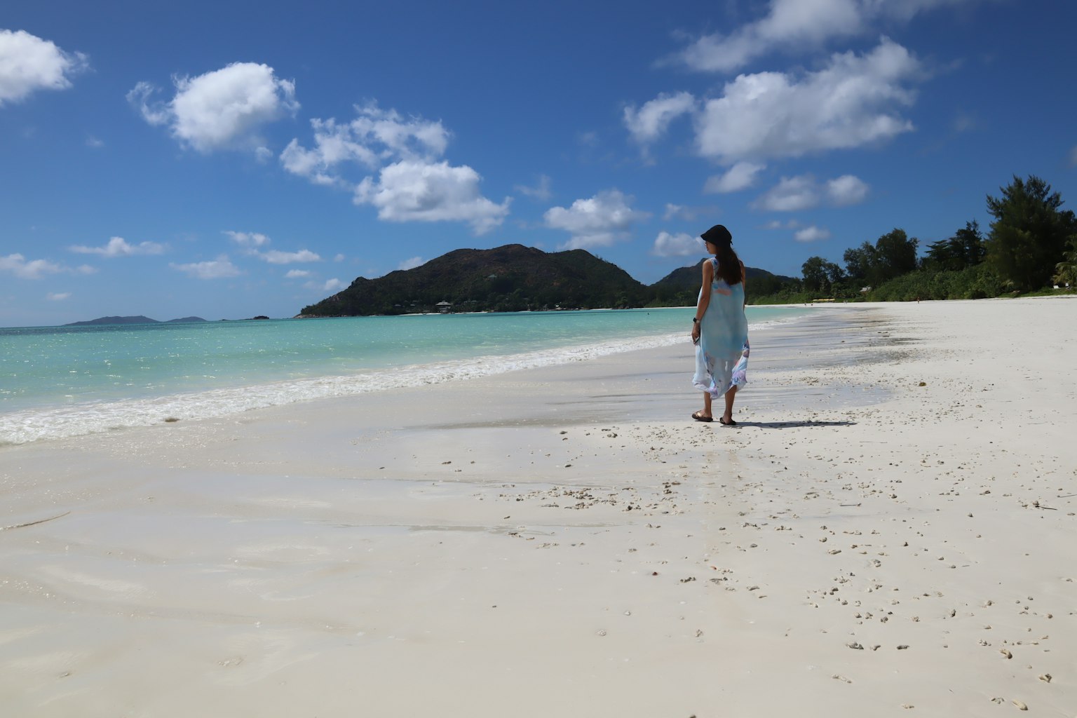 Femme marchant sur une plage de sable blanc avec océan bleu et nuages