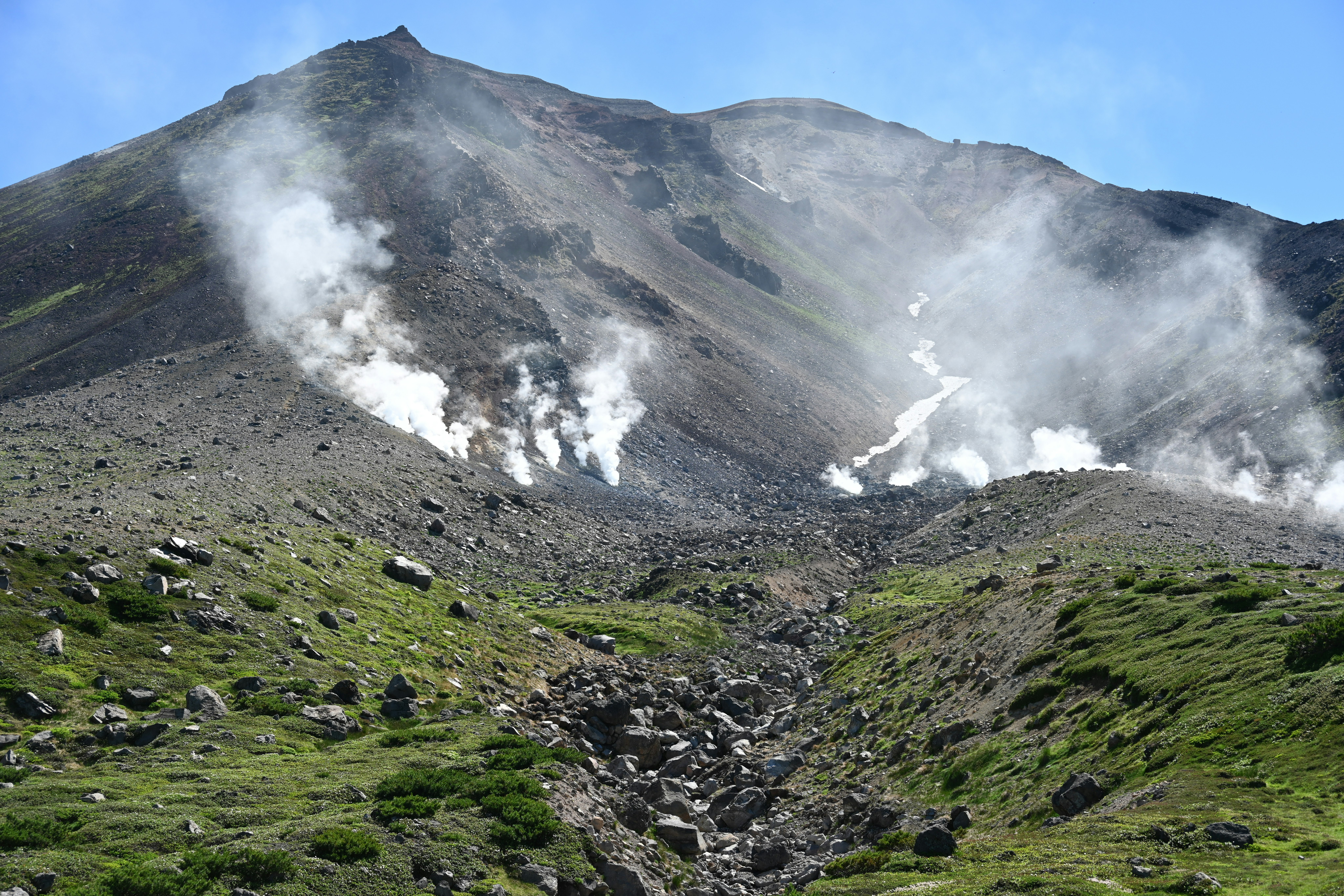噴煙を上げる火山と緑の山腹の景観