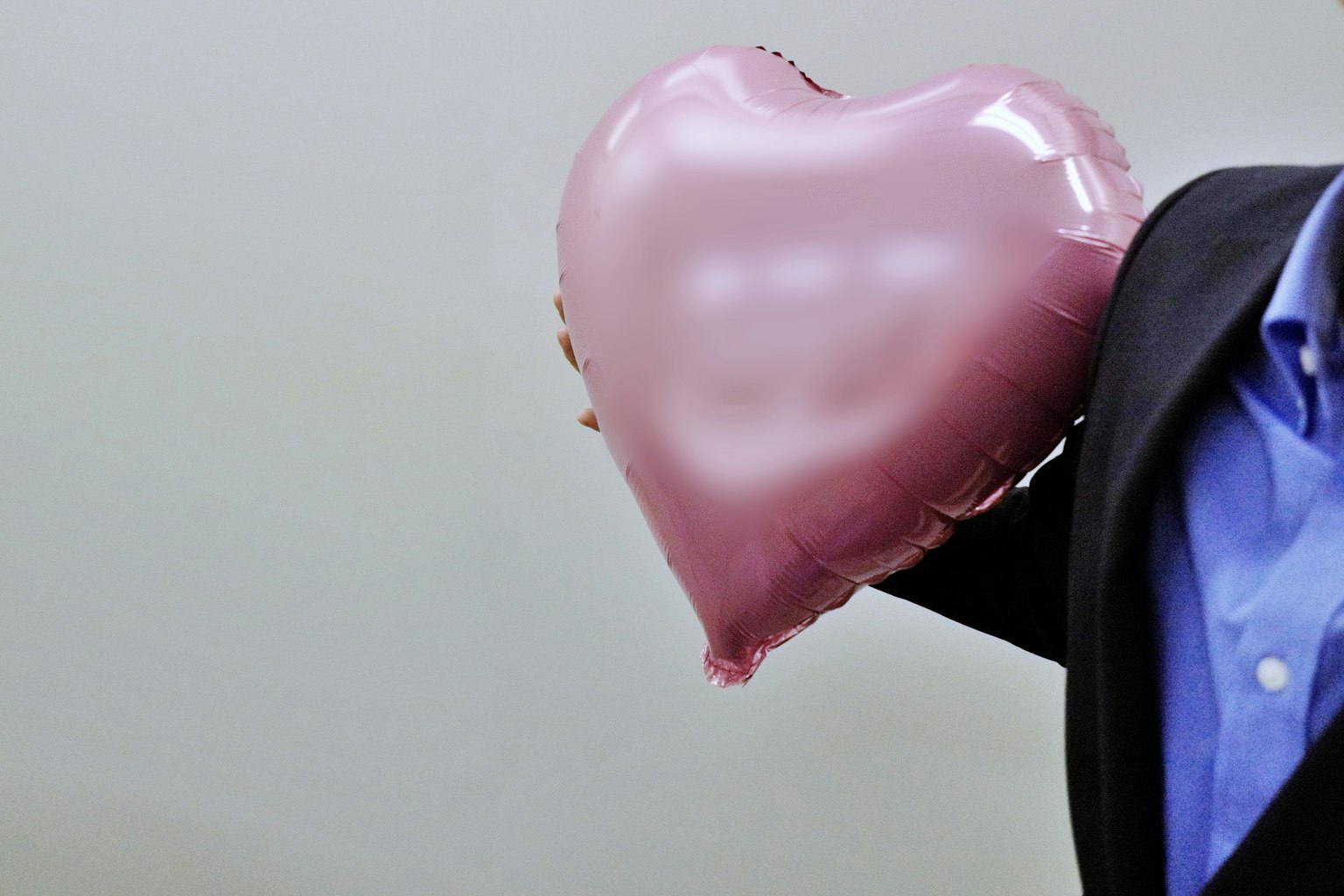 Pria berpakaian jas memegang balon berbentuk hati berwarna pink